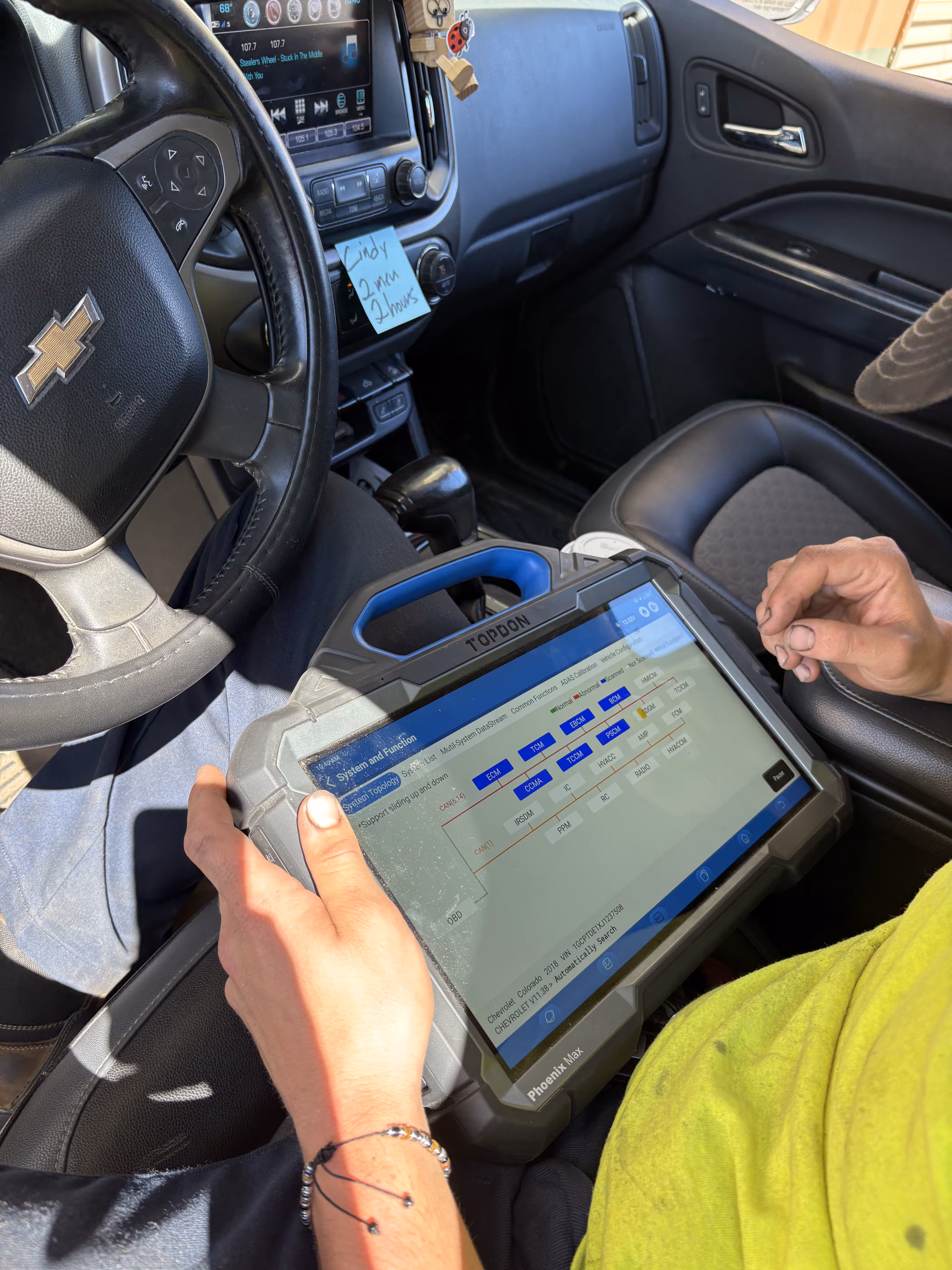 A technician runs a scan tool on a Chevrolet pickup's control modules from inside the cab