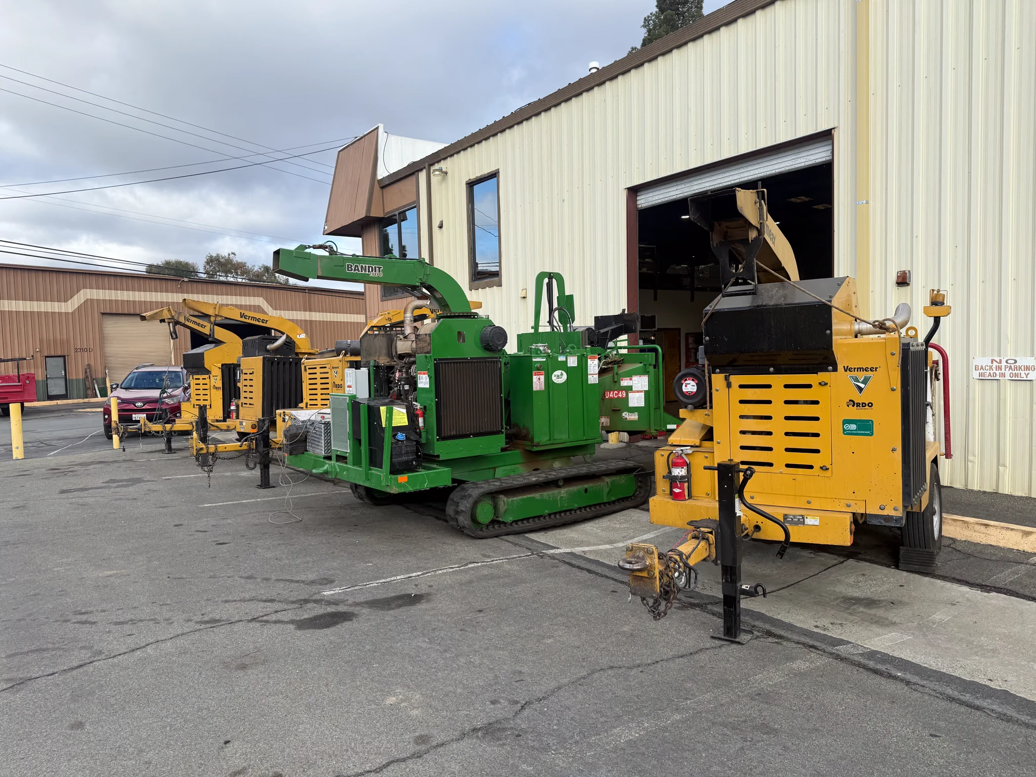 Bandit and Vermeer wood chippers lined up outside an open shop bay door
