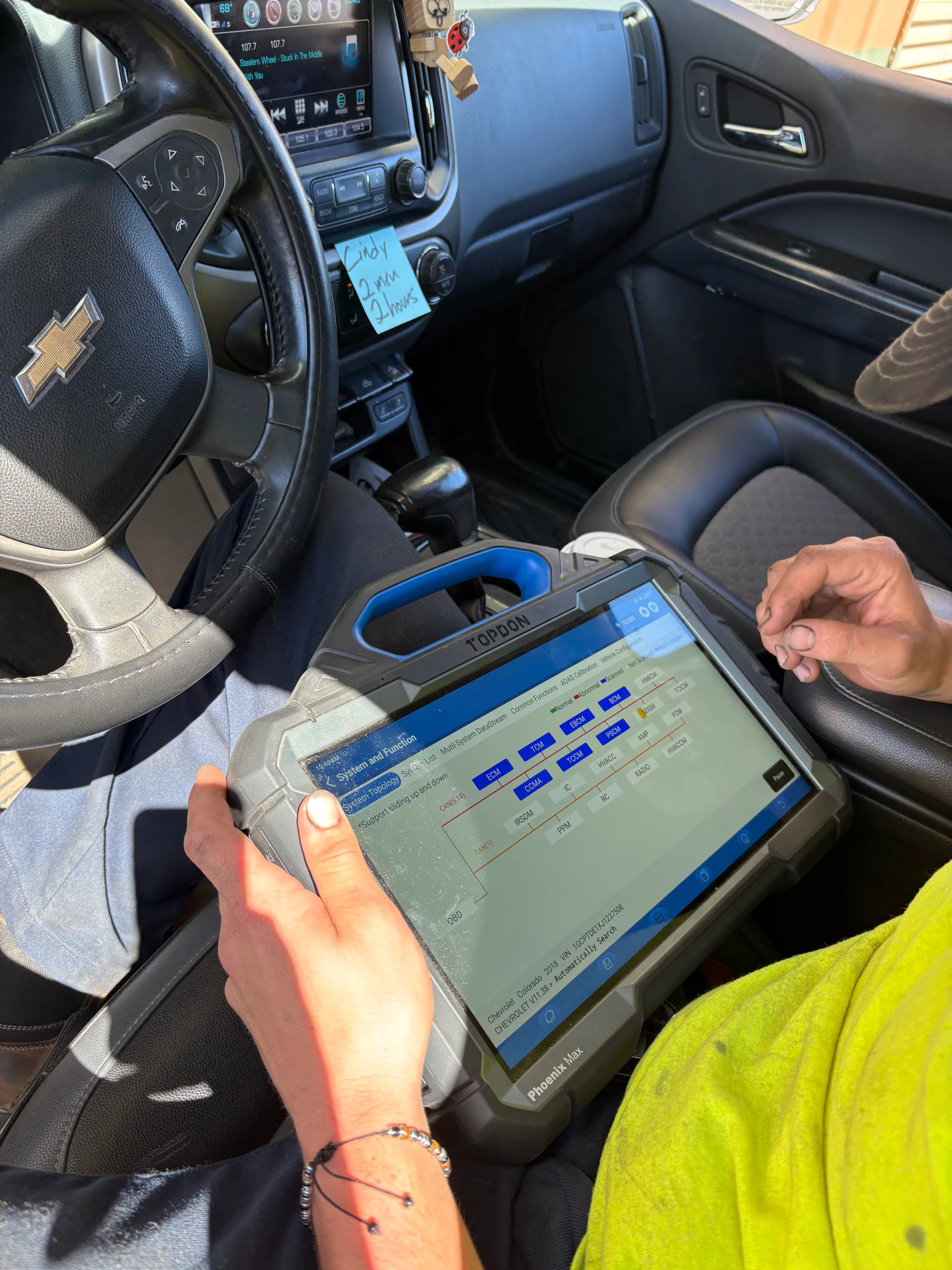 A technician runs a scan tool on a Chevrolet pickup's control modules from inside the cab