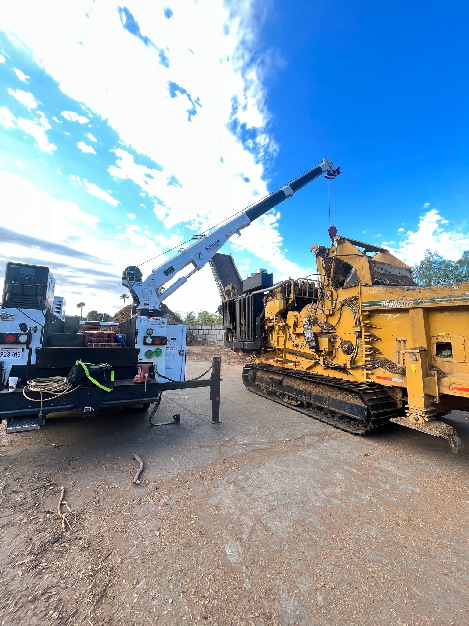 A service truck with a Stellar crane parked beside a yellow tracked grinder marked HG8000TX