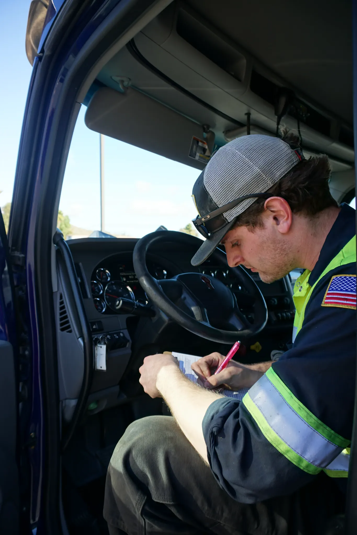 A technician sits in the cab of a heavy truck filling out an inspection sheet on a clipboard