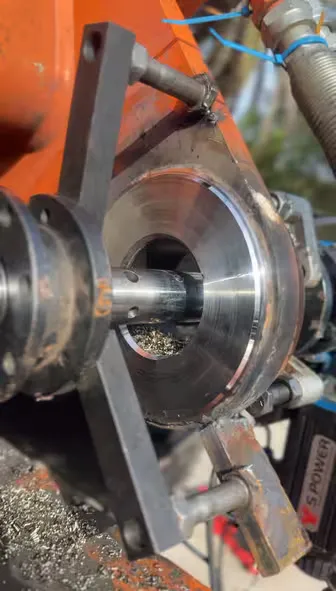 Portable line-boring bar set up through a freshly machined bore on orange heavy equipment outdoors