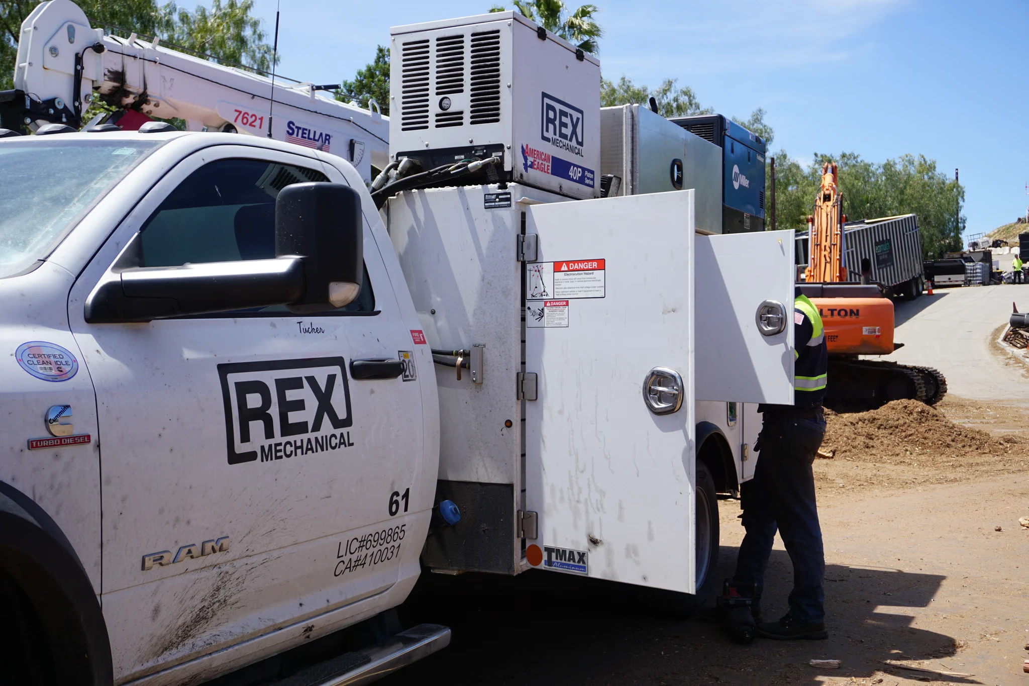 REX Mechanical service truck with its body doors open beside a tracked excavator on a dirt jobsite