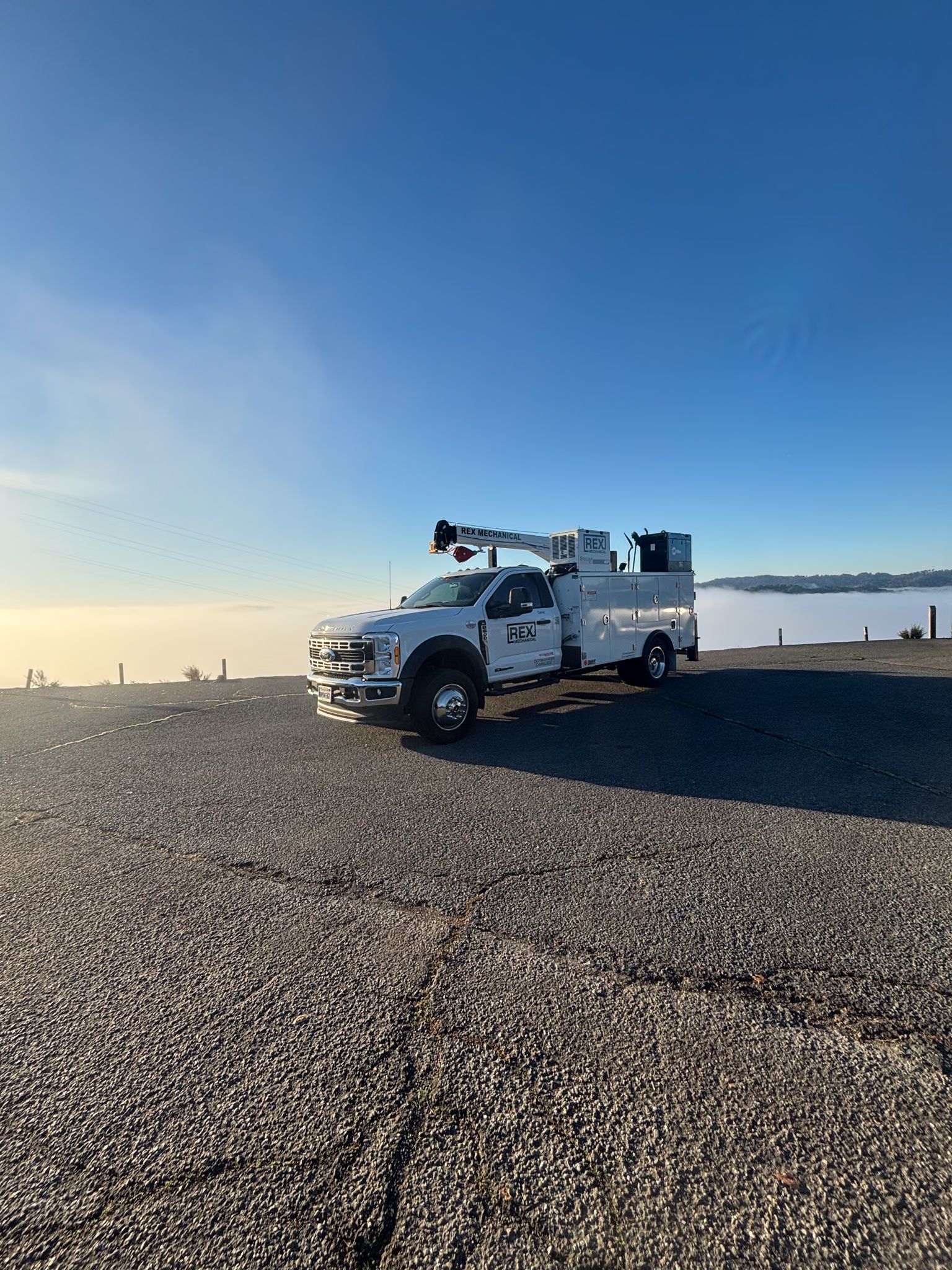 REX Mechanical service truck with a bed crane parked at a paved overlook above morning fog