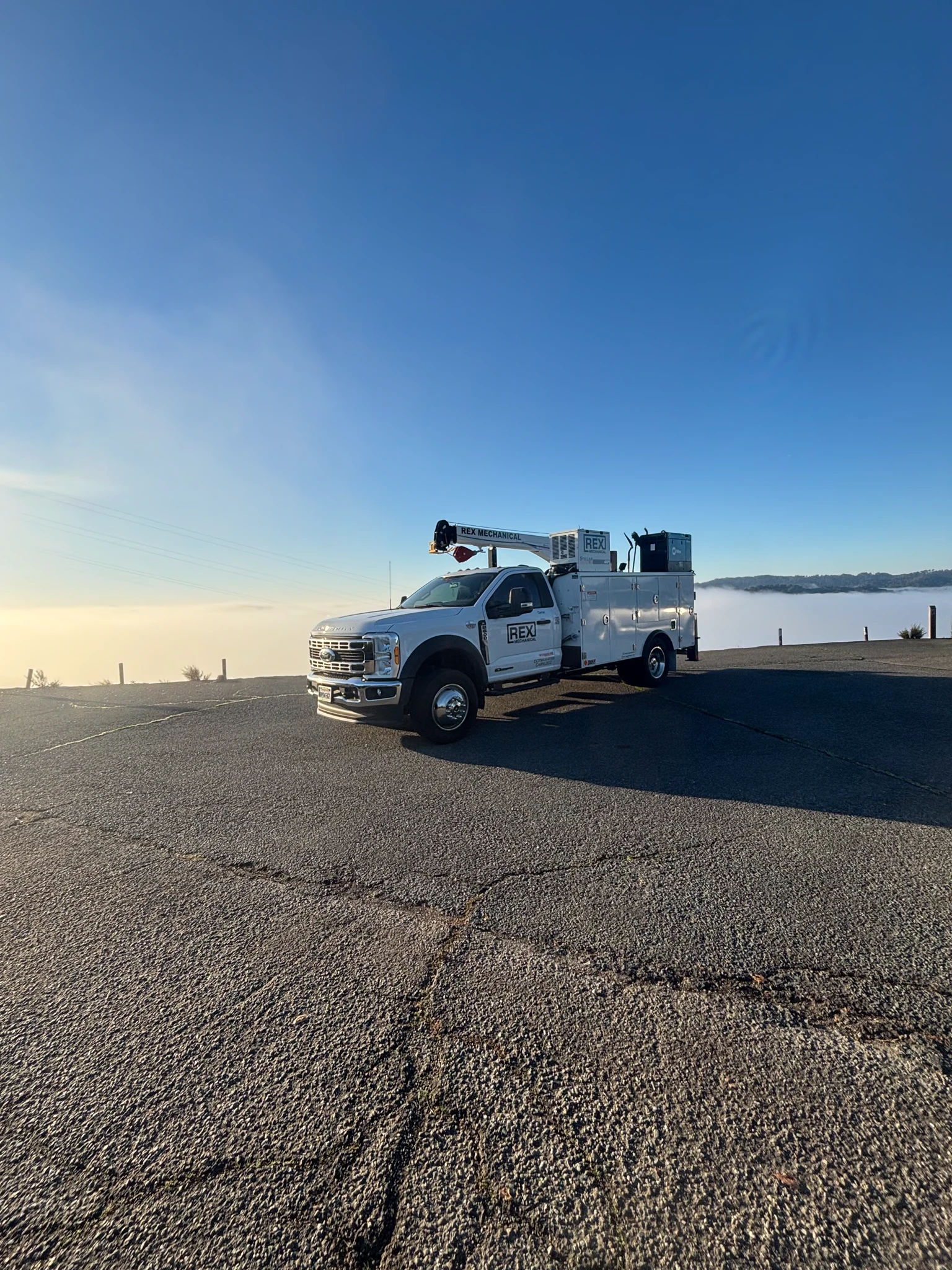 REX Mechanical service truck with a bed crane parked at a paved overlook above morning fog