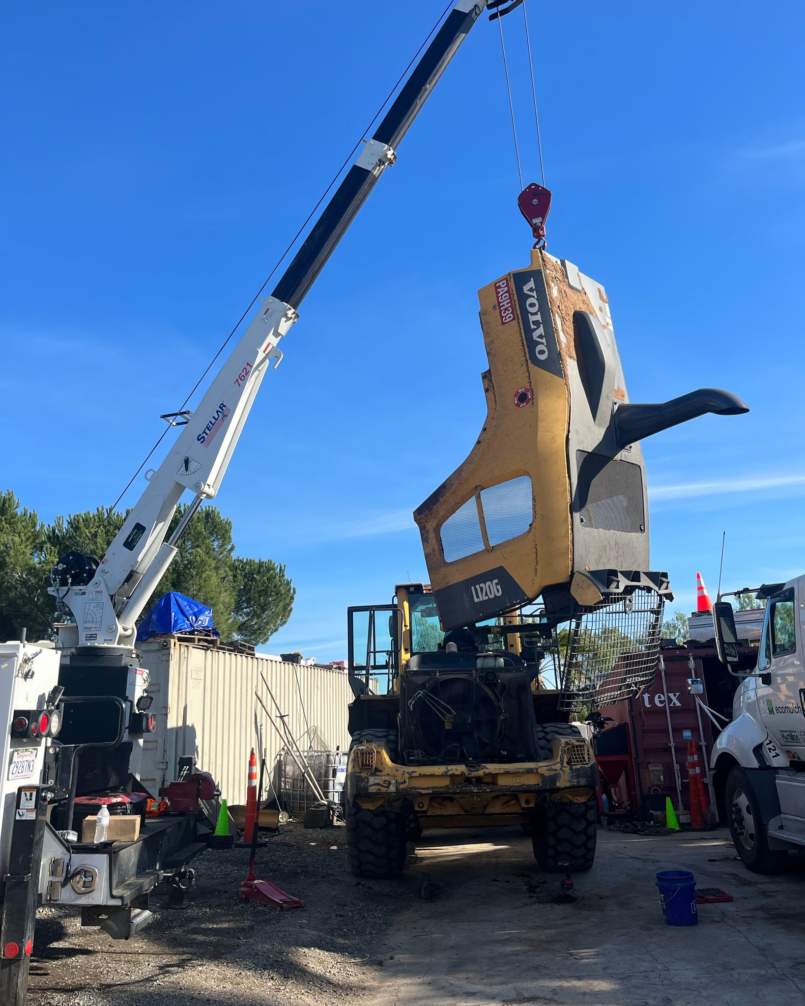 A truck-mounted crane lifts the engine hood off a Volvo L120G wheel loader in the yard